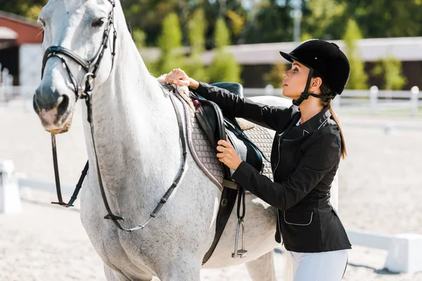 Atraente fêmea equestre fixação cavalo sela no clube de cavalos — Stock Photo