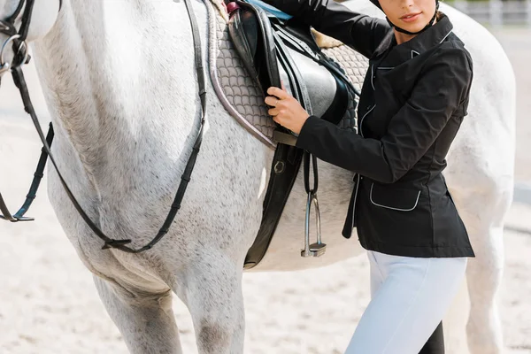 Cropped image of female equestrian fixing horse saddle at horse club — Stock Photo