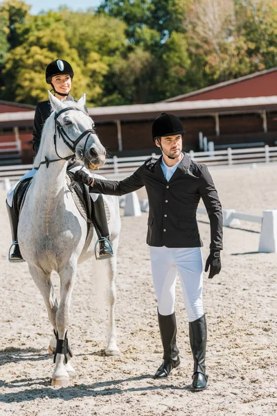 Handsome male equestrians holding horse halter, female jockey sitting on horse at horse club — Stock Photo