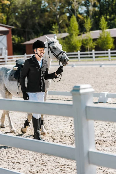 Sorridente bonito masculino equestre andando perto de cavalo no clube de cavalos — Stock Photo