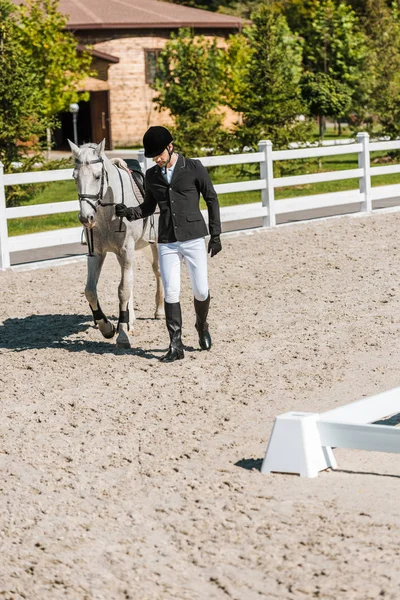 Bonito masculino equestre no profissional vestuário andando perto de cavalo no cavalo clube — Fotografia de Stock