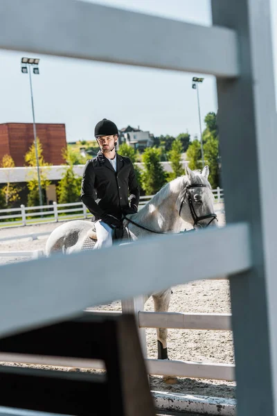 Blick durch Zaun auf gut aussehenden Jockey, der Schimmel im Pferdeclub reitet — Stockfoto