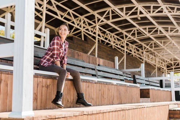 Sonriente hermosa mujer en ropa casual sentado en el banco en el estadio rancho - foto de stock