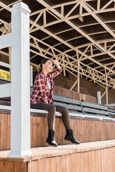 Attraktives Cowgirl im karierten Hemd sitzt auf Bank im Ranch Stadium und schaut sich etwas an — Stockfoto