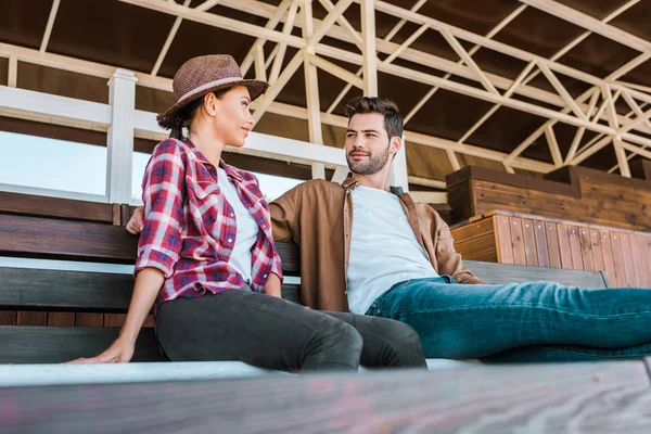 Equestrians in casual clothes sitting on bench at ranch stadium and looking at each other — Stock Photo