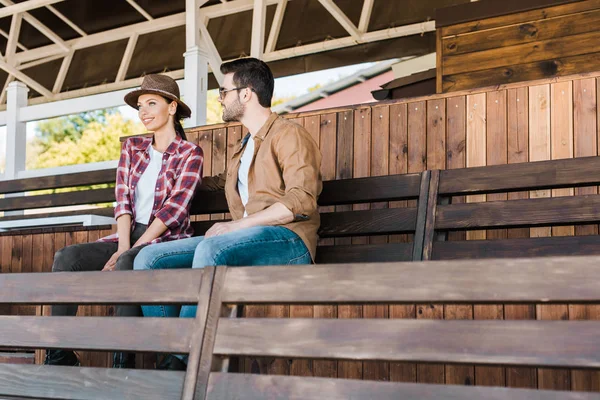 Alegre vaquero y vaquera en ropa casual sentado en el banco en el estadio del rancho - foto de stock