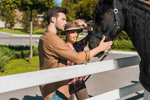 Female and male equestrians palming black horse at ranch — Stock Photo