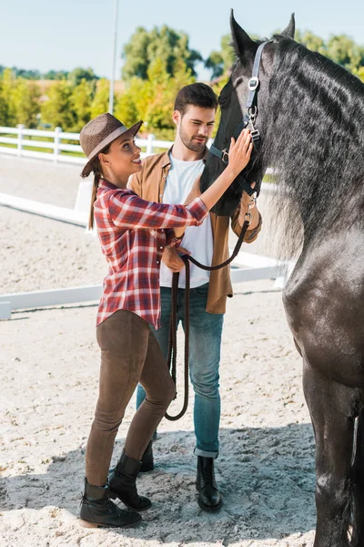 Jinetes femeninos y masculinos palmando caballo negro en el rancho - foto de stock