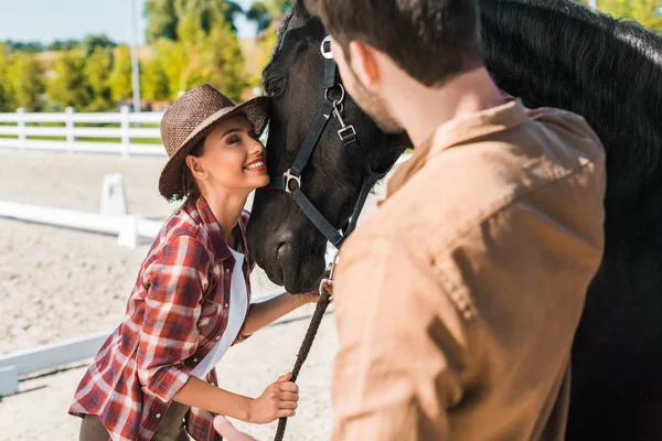 Bella equestre in cappello che abbraccia cavallo nero al ranch — Foto stock