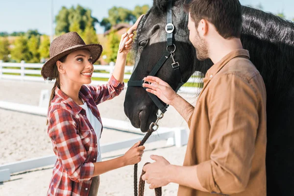 Alegre vaquero y vaquera mirándose el uno al otro cerca del caballo en el rancho - foto de stock