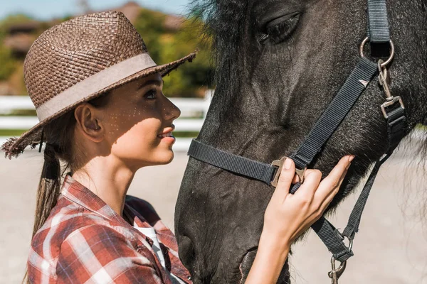 Porträt einer attraktiven Reiterin, die das Pferd auf der Ranch berührt und betrachtet — Stockfoto