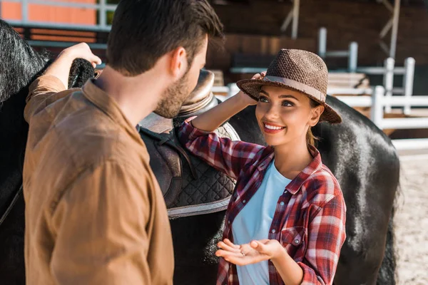 Vaquero y vaquera de pie cerca de caballo y hablando en el rancho - foto de stock