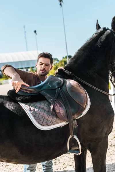 Handsome cowboy fixing horse saddle at ranch — Stock Photo