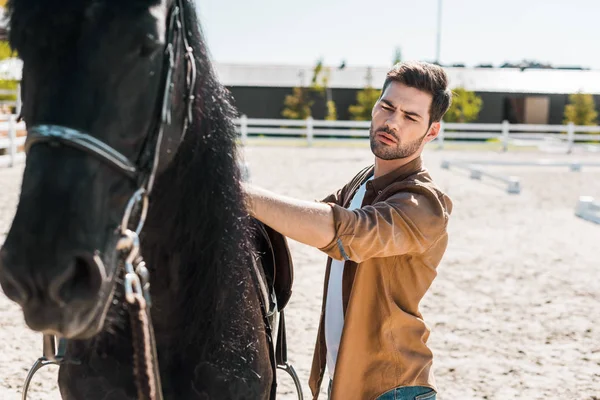 Handsome serious cowboy fixing horse saddle at ranch — Stock Photo