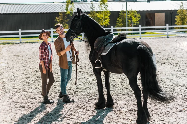 Smiling female and male equestrians standing with horse at ranch — Stock Photo