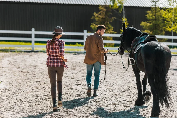 Rückansicht von Cowboy und Cowgirl, die mit schwarzem Pferd auf Ranch gehen — Stockfoto