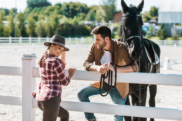 Cow-boy souriant et cow-girl debout près de la clôture avec cheval et parlant au ranch — Photo de stock