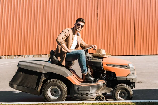 Bello cowboy in abiti casual e occhiali da sole equitazione ranch veicolo vicino edificio — Foto stock