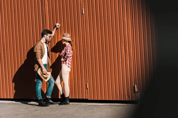 Man and woman in casual clothes leaning on brown wall and looking at each other at ranch — Stock Photo