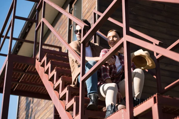 Vaquero y vaquera en ropa casual sentado en la escalera en el rancho - foto de stock