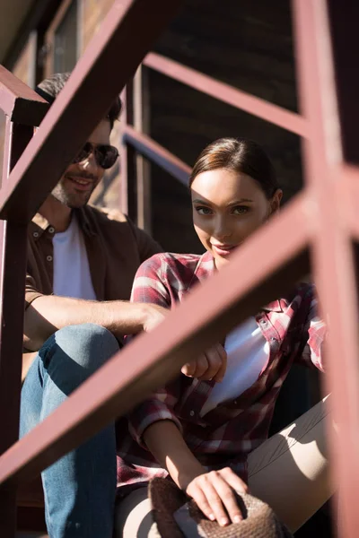 Vista através de cerca homem e mulher em roupas casuais sentado na escada no rancho — Fotografia de Stock