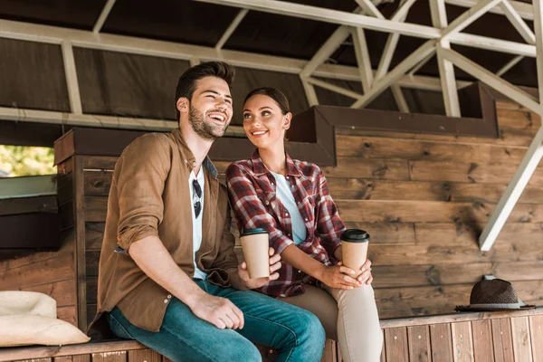 Улыбающиеся мужчина и женщина сидят с одноразовыми чашками кофе на ранчо — стоковое фото