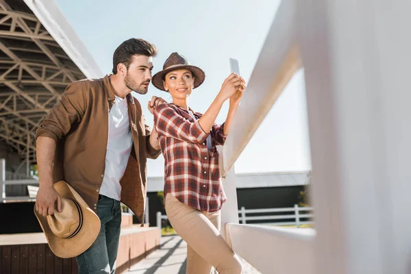 Messa a fuoco selettiva di equestri alla moda in abiti casual scattare selfie con smartphone al ranch — Foto stock