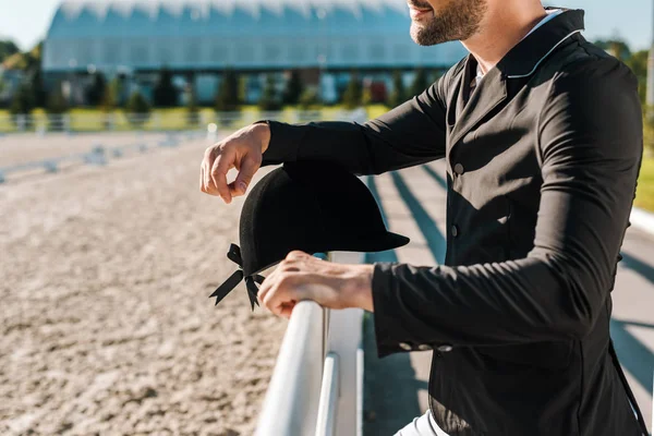 Imagem cortada de masculino equestre inclinando-se na cerca com capacete de equitação no clube de cavalos — Fotografia de Stock