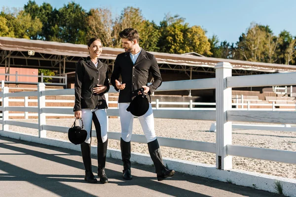 Lächelnde Reiter in professioneller Kleidung gehen am Zaun entlang und unterhalten sich auf der Ranch — Stockfoto