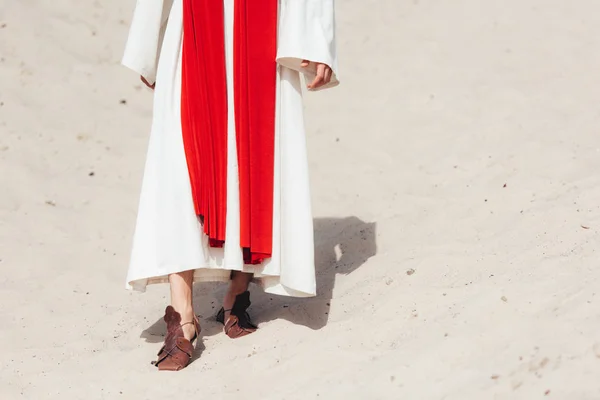 Cropped image of Jesus in robe, red sash and sandals walking on sand in desert — Stock Photo