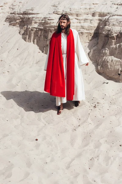 Jesus in robe, red sash and crown of thorns walking in desert — Stock Photo