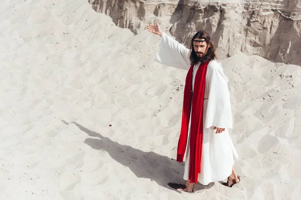 High angle view of Jesus in robe, red sash and crown of thorns showing way in desert — Stock Photo