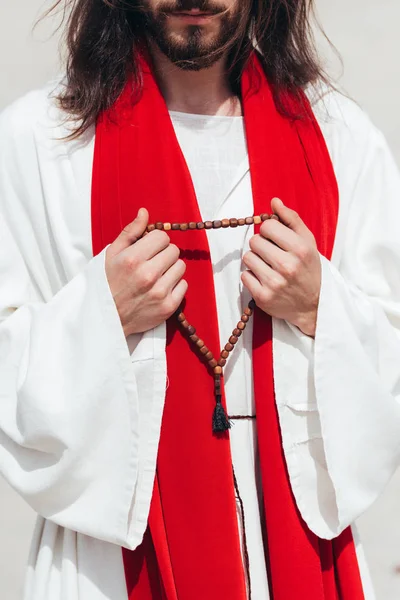Cropped image Jesus in robe and red sash holding wooden rosary in desert — Stock Photo
