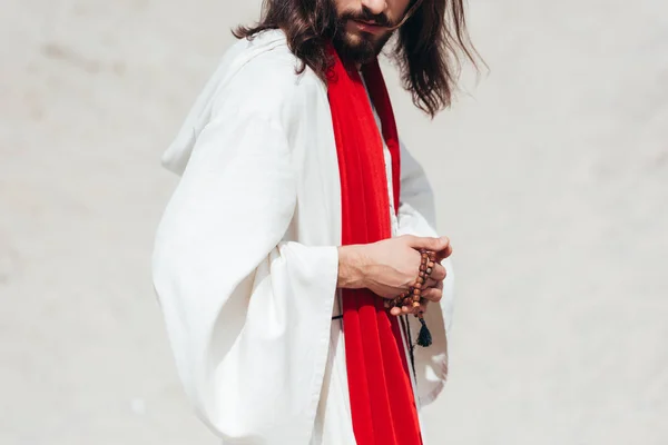 Cropped image Jesus in robe and red sash holding rosary in desert — Stock Photo