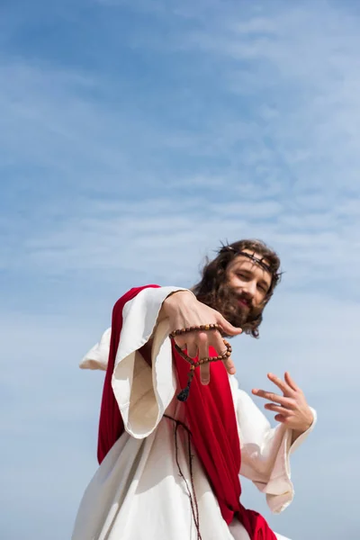 Low angle view of Jesus having fun and showing two fingers with rosary against blue sky — Stock Photo