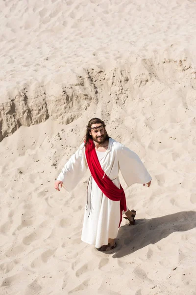High angle view of Jesus in robe, red sash and crown of thorns walking on sand in desert — Stock Photo