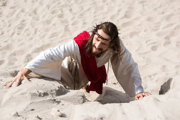 High angle view of Jesus in robe and crown of thorns climbing sandy hill in desert — Stock Photo