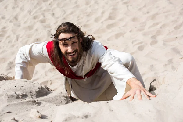 Vista de ángulo alto de Jesús sonriente subiendo colina arenosa en el desierto y mirando a la cámara - foto de stock