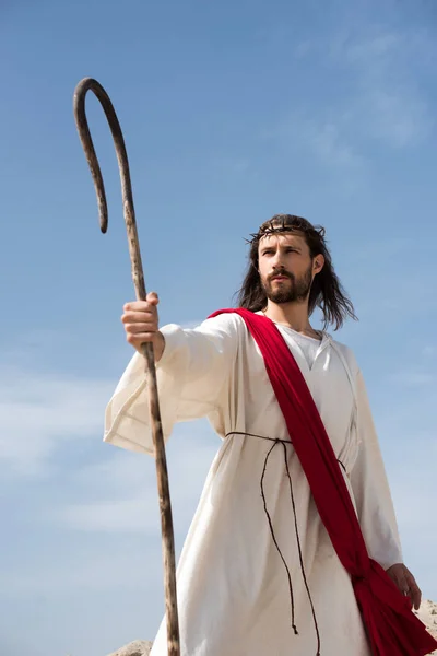 Jesus in robe, red sash and crown of thorns standing with wooden staff in desert — Stock Photo