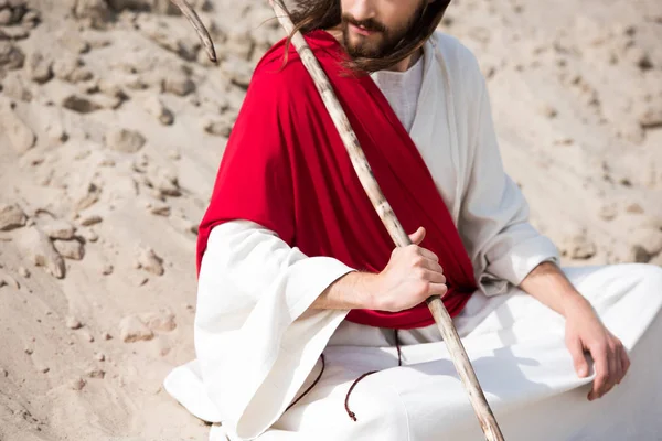 Cropped image of Jesus in robe, red sash and crown of thorns sitting in lotus position on sand in desert — Stock Photo