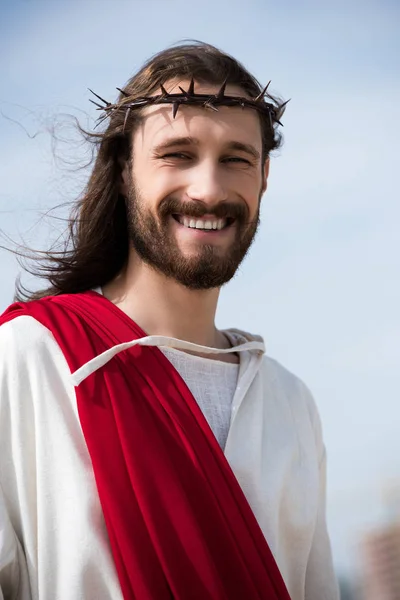 Retrato de Jesús sonriente en túnica, faja roja y corona de espinas al aire libre - foto de stock