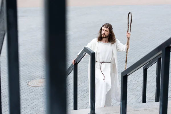 High angle view of Jesus in robe and crown of thorns walking on stairs with staff — Stock Photo