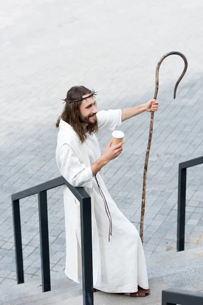 Высокий угол зрения Иисуса в халате и терновом венце с одноразовой чашкой кофе и сотрудниками на улице — стоковое фото