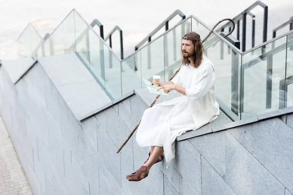 Jesus in robe and crown of thorns sitting on staircase side and pointing on map — Stock Photo
