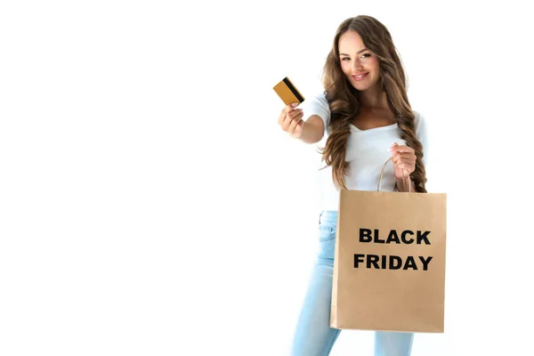 Chica feliz sosteniendo tarjeta de crédito de oro y bolsa de compras con signo de viernes negro, aislado en blanco - foto de stock