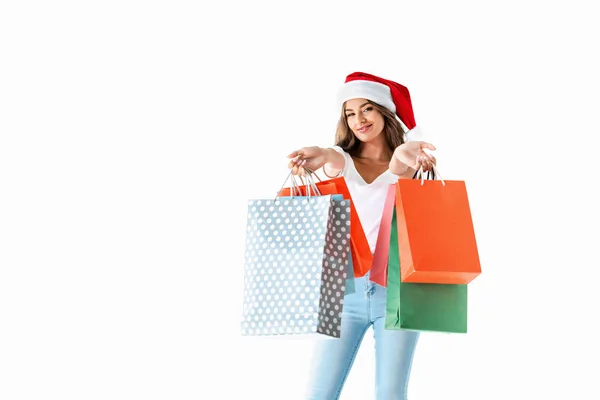 Atractiva chica sonriente en santa hat sosteniendo bolsas de compras, aislado en blanco - foto de stock