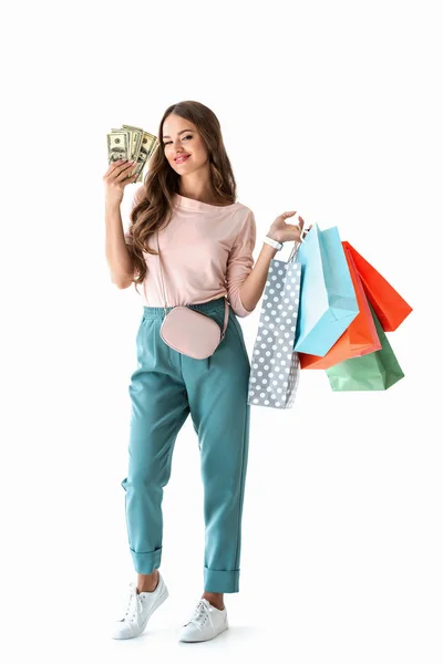 Atractiva chica alegre sosteniendo billetes de dólar y bolsas de compras, aislado en blanco - foto de stock