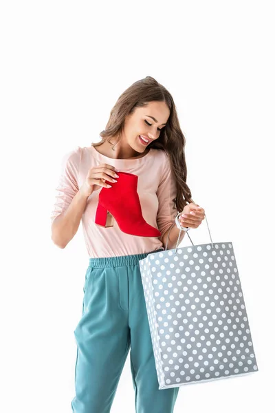 Усміхнена дівчина з сумкою для покупок і червоним взуттям, ізольована на білому — стокове фото