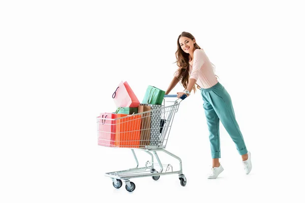 Bela menina alegre com carrinho de compras e sacos, isolado em branco — Fotografia de Stock