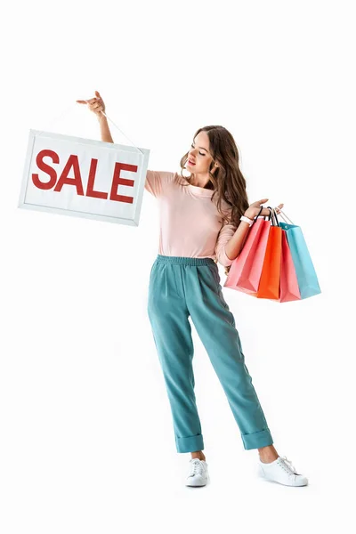 Cropped view of brunette young woman holding board with sale sign and shopping bags, isolated on white — Stock Photo